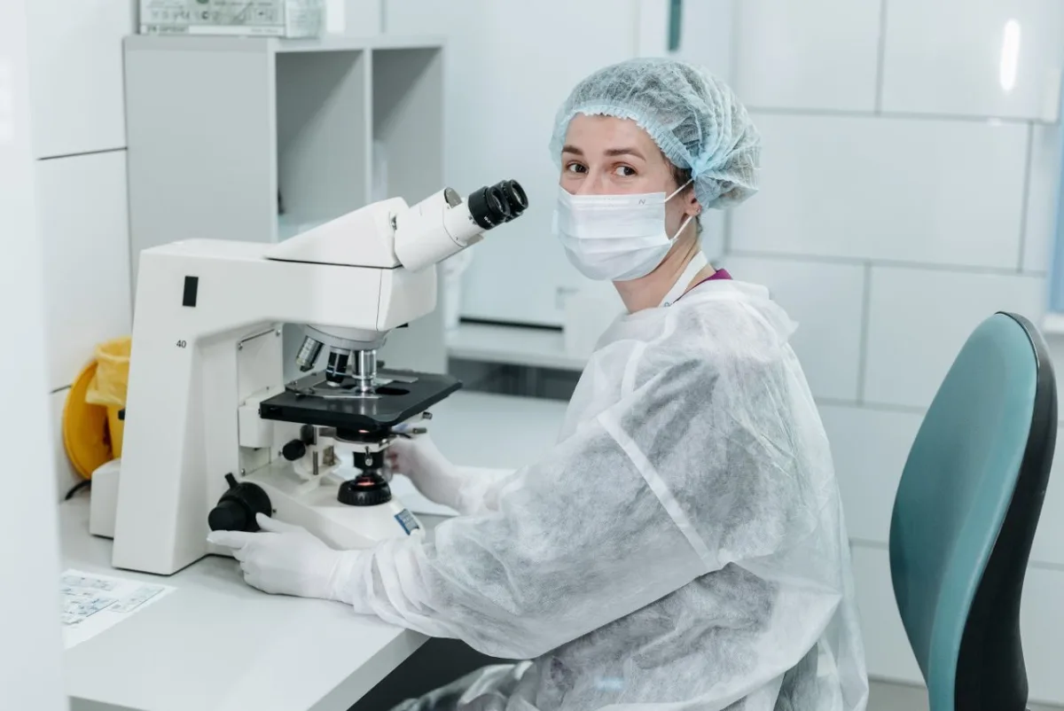 Lab technician with microscope in cleanroom-style setting