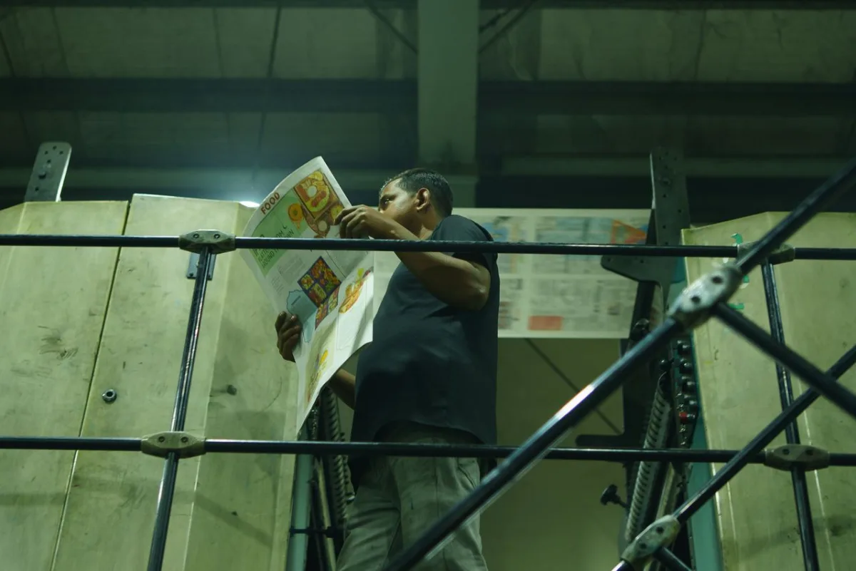 Factory worker inspecting a printed sheet on press