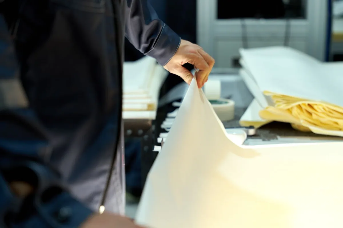 Factory worker inspecting a large thin paper sheet on the line